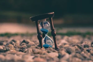 An hourglass with blue sand slowly trickles down as it rests on a bed of pebbles, symbolizing the passage of time. Time and patience are key to successful SEO; let's work together to accelerate your results.